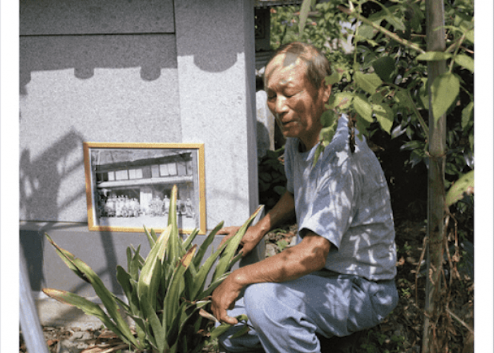 Ryuji Niwata posant dans le jardin de sa maison au côté du lys sacré du Japon qui figure sur la photographie prise le lendemain de la mort de Shozo Tanaka en septembre 1913 - Sano, préfecture de Tochigi, 2018. Crédit photo : Alexia Duchange.